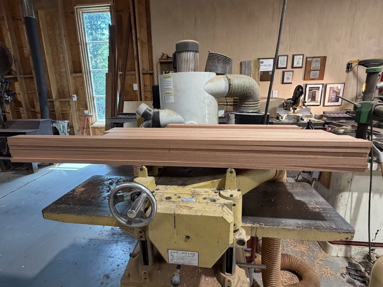 Woodworking shop with a large woodworking machine and several stacked wooden planks.