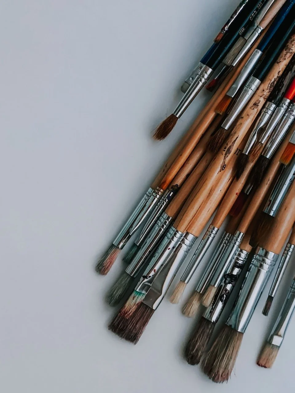 A variety of paintbrushes with wooden handles and different bristle shapes, laid out on a white surface.