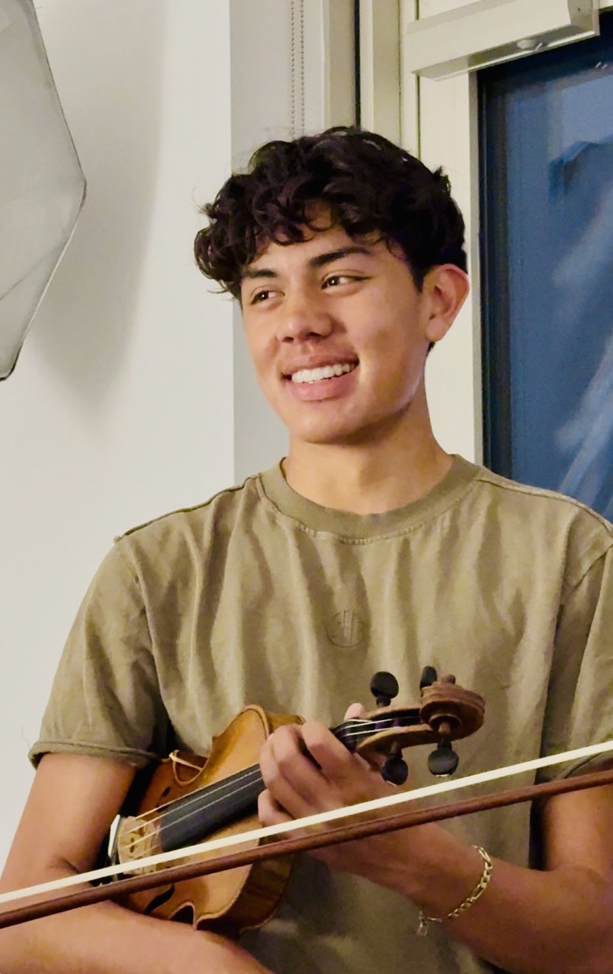 Young man with curly hair smiling while holding a violin and a bow