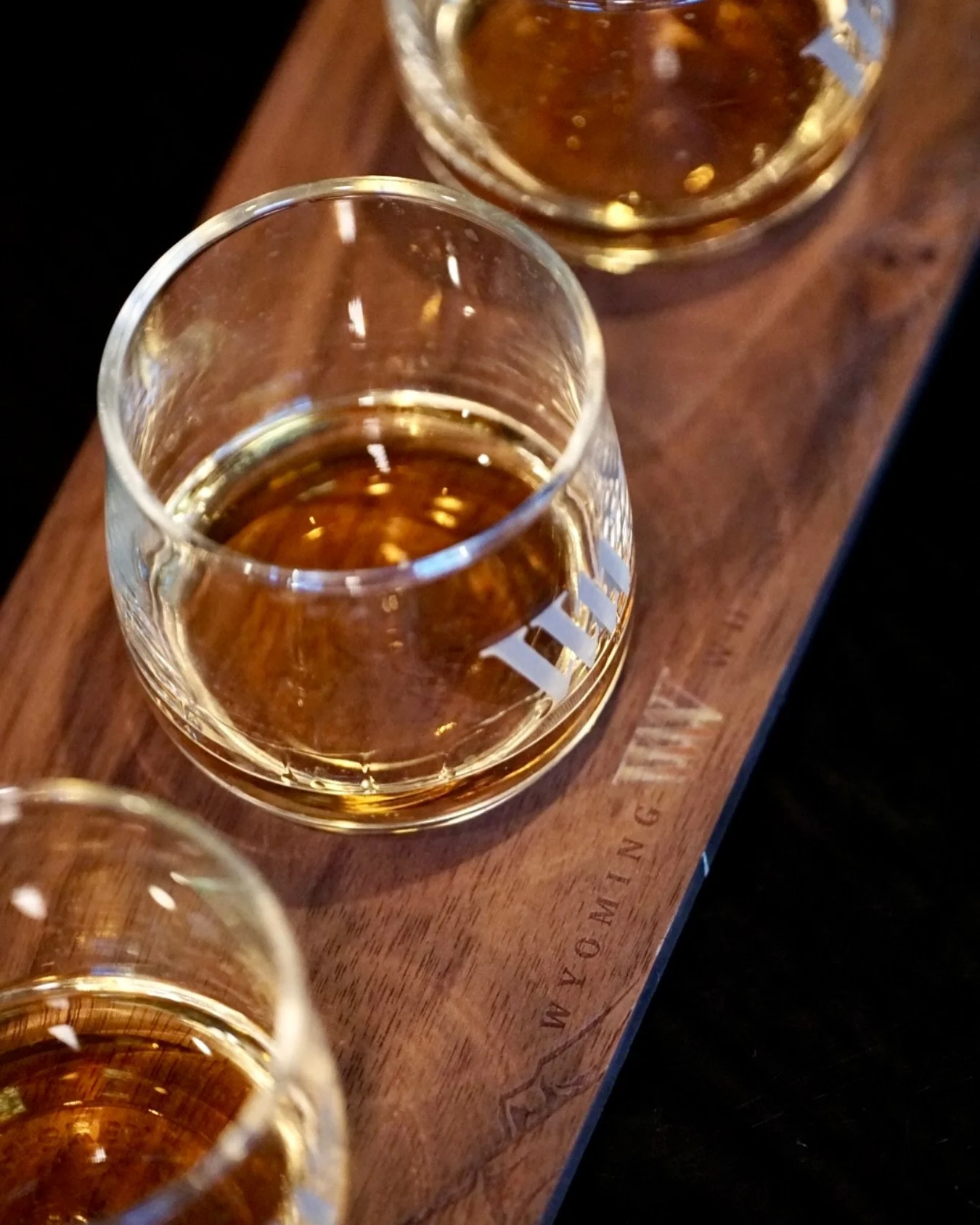 Close-up view of several glasses of whiskey on a wooden tasting board.