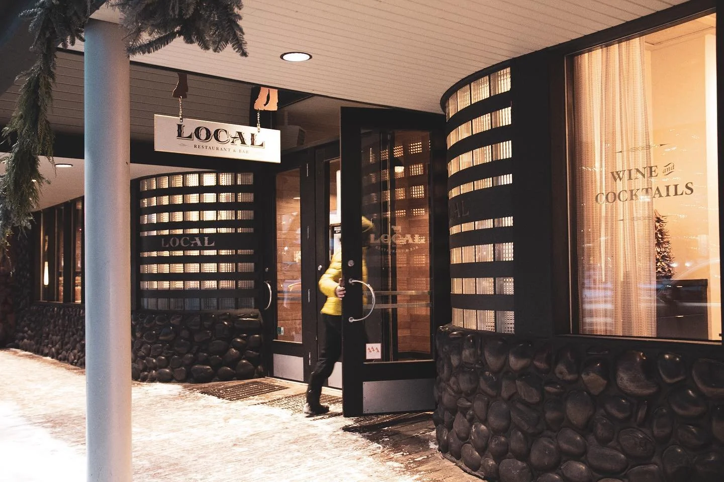 Entry door of a restaurant named 'Local' with a person in a yellow jacket entering, and signs indicating wine and cocktails, and the restaurant's name.
