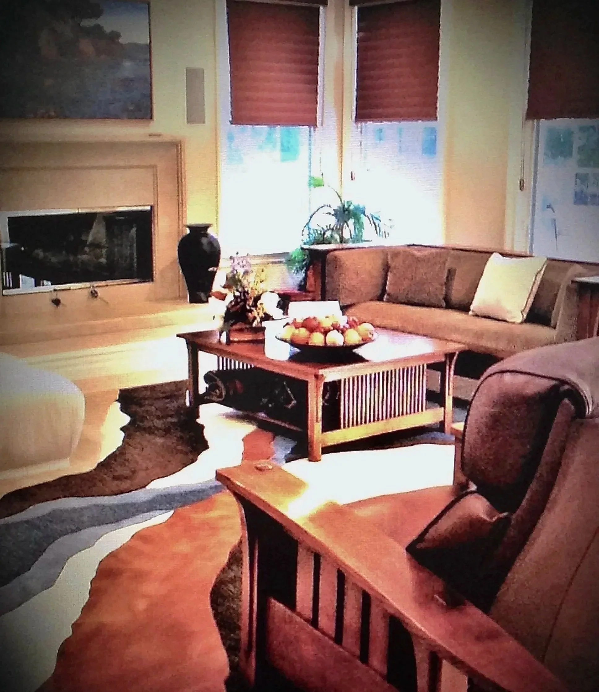 Living room with yellow walls, large window covered with red blinds, framed artwork on the wall, fireplace, brown sofa, and wooden coffee table with decorative items, plants, and fruit bowl.