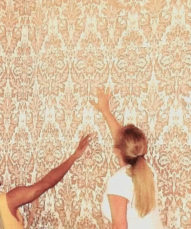 Two designers applying  patterned fabric wallcovering.