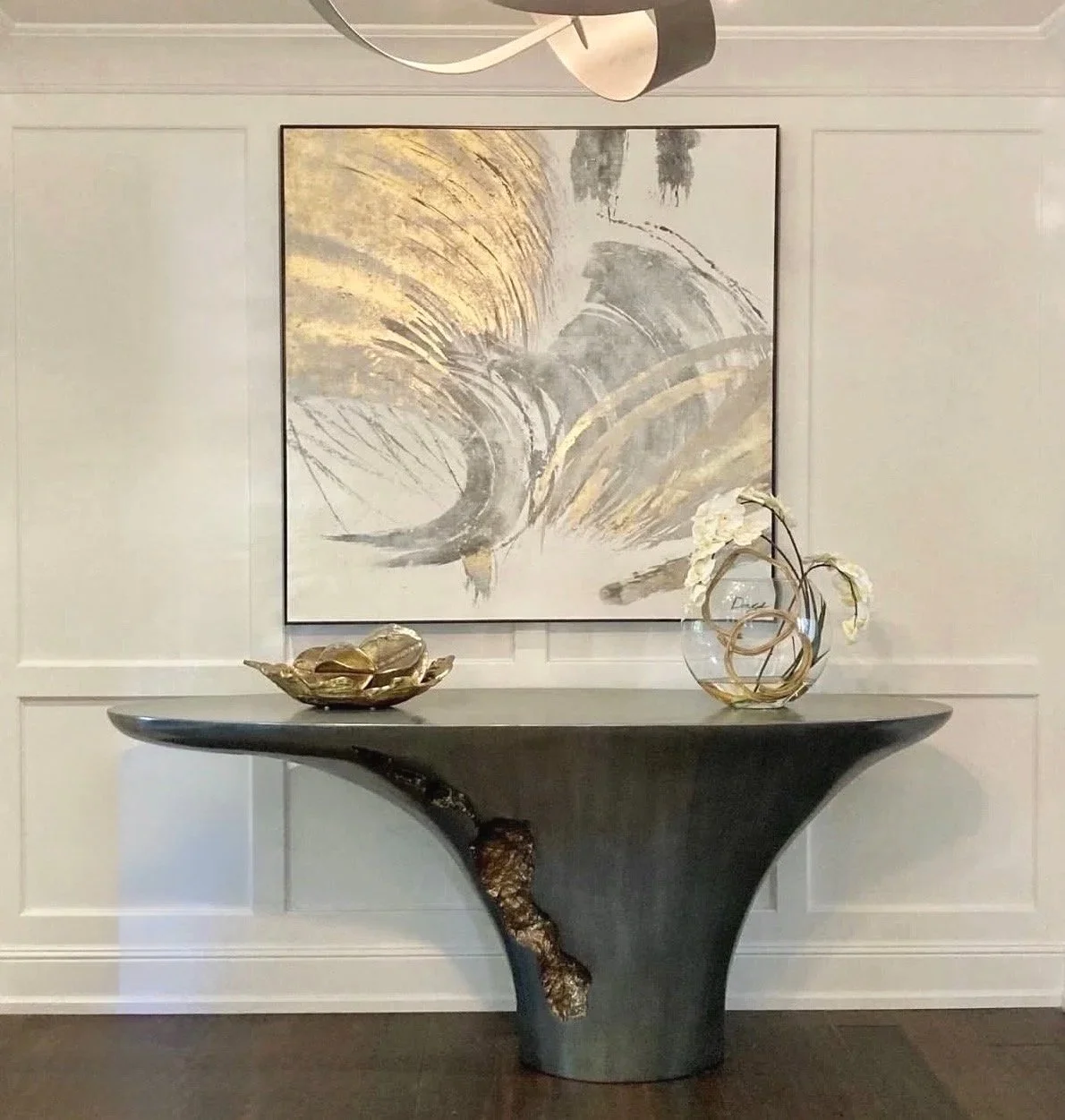 Decorative black table with gold accents, placed against a white paneled wall, with abstract art and gold and white vases on top.