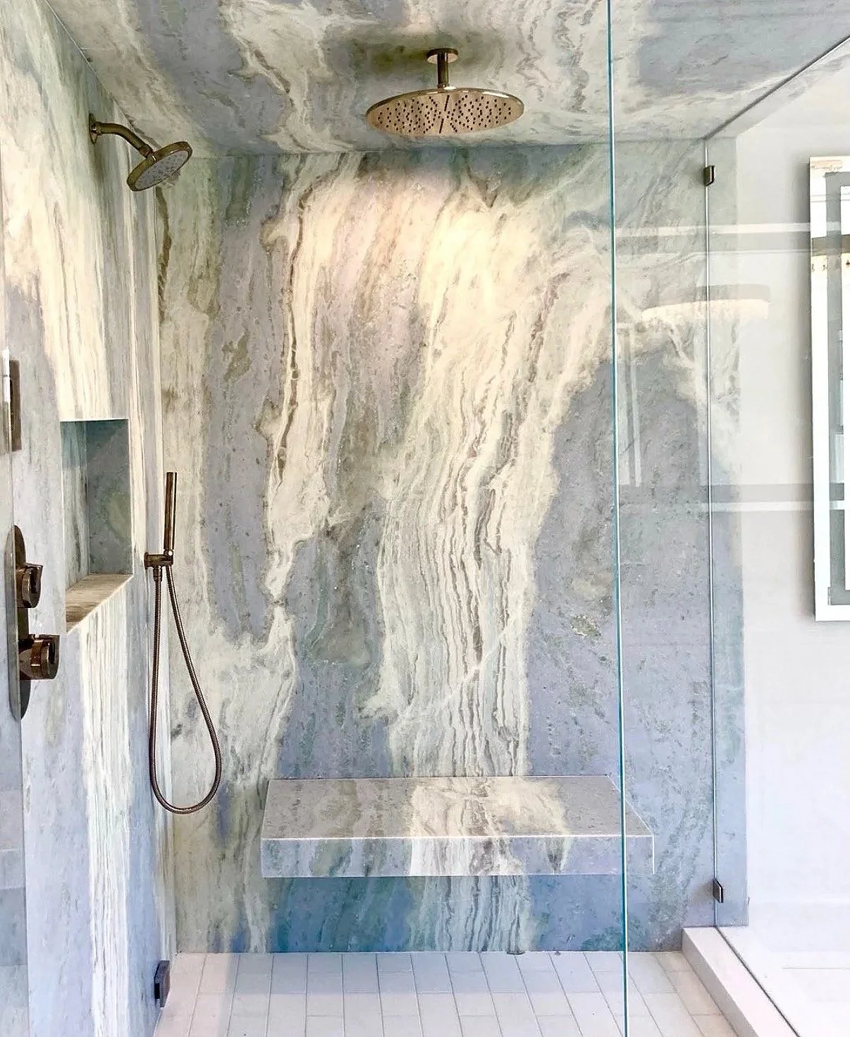 Modern walk-in shower with marbled stone walls, a built-in bench, dual showerheads, and a glass enclosure.