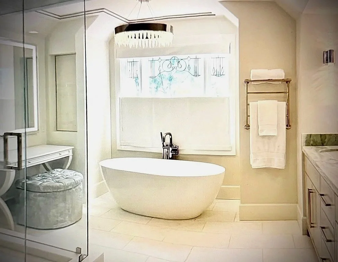 A luxurious bathroom featuring a freestanding bathtub with a black faucet in front of a window, with a glass shower enclosure to the left, a vanity with a marble countertop on the right, and a towel rack mounted on the wall.