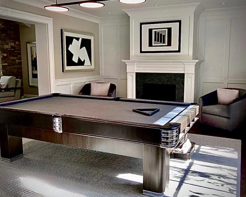 A pool table in a living room with modern decor, artwork on walls, a fireplace, and chairs.