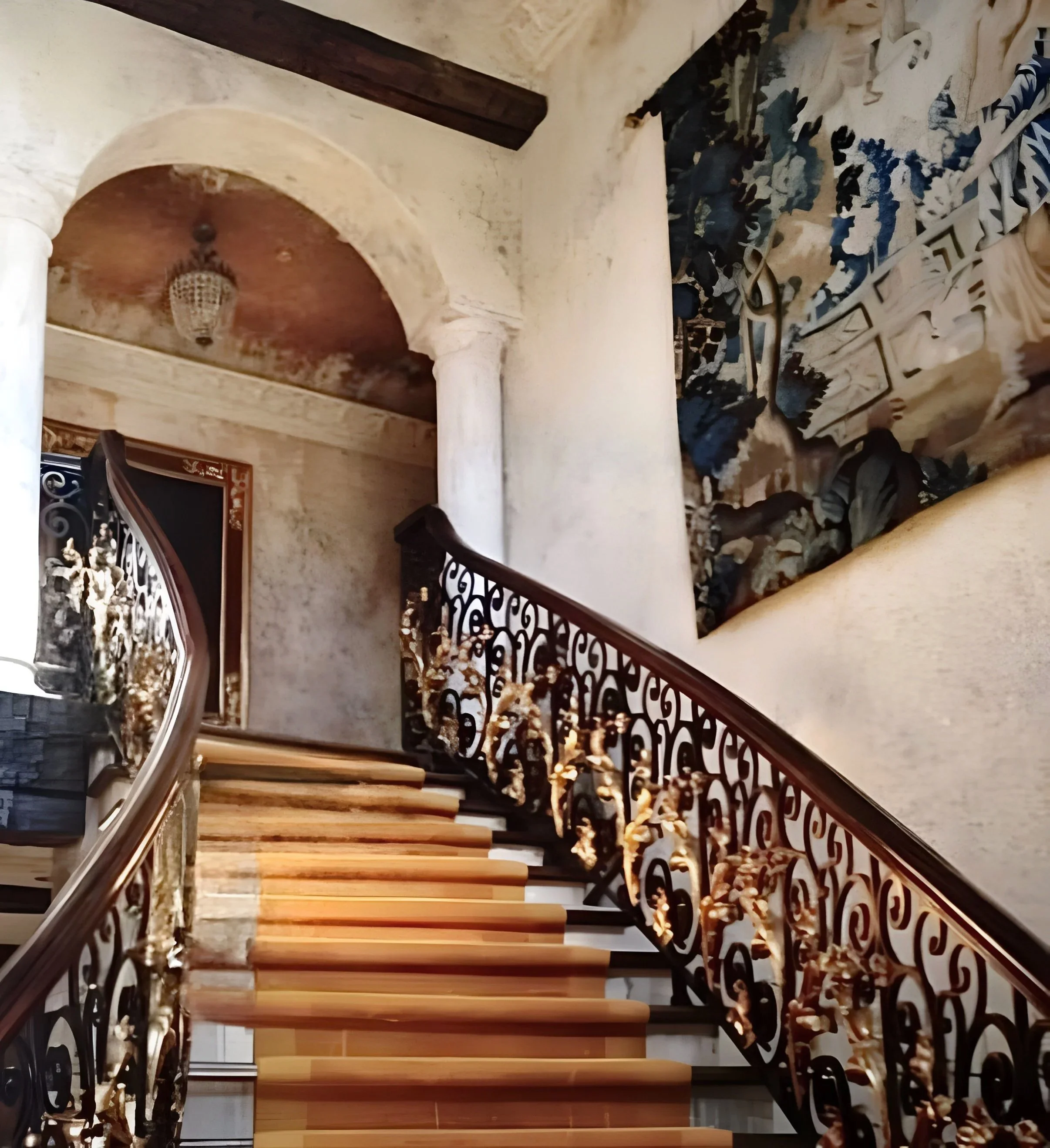 Interior view of a staircase with wooden steps, ornate black metal railings, and a wall with peeling paint and decorative elements.