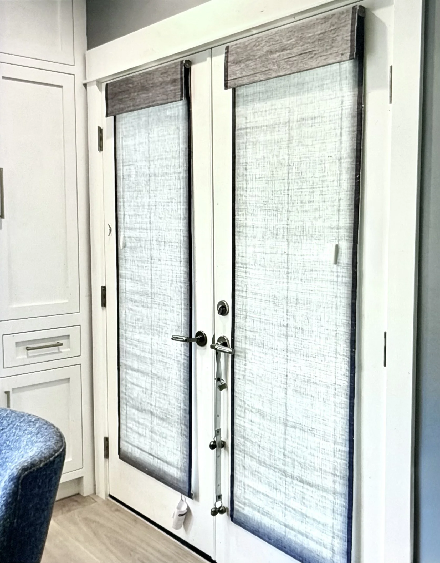Double glass door with black frames and handles, with a steering wheel and pendants hanging from the handles, set in a kitchen with white cabinetry and gray walls.