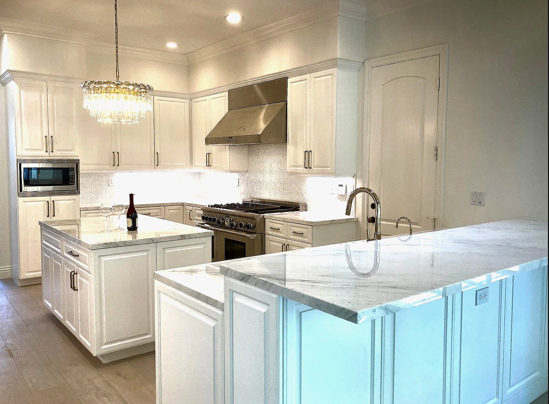 Bright kitchen with white cabinets, marble countertops, stainless steel appliances, a chandelier, and a wine bottle on the island.