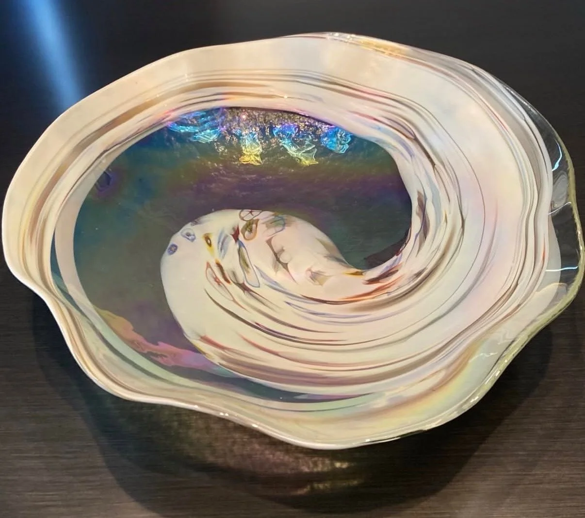 A decorative glass bowl with swirling rainbow-like patterns, resting on a dark surface.