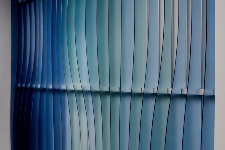 Close-up view of curved blue and teal metal panels arranged in parallel with reflections.