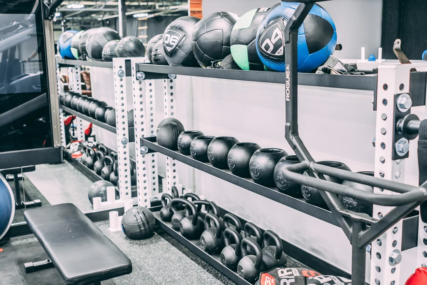 Functional training area with kettlebells, medicine balls, adjustable bench, and organized gym storage system
