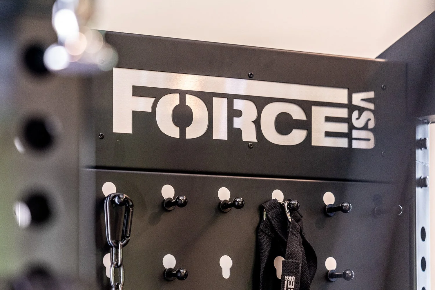Force USA gym storage panel with hooks holding fitness accessories in modern home gym setup
