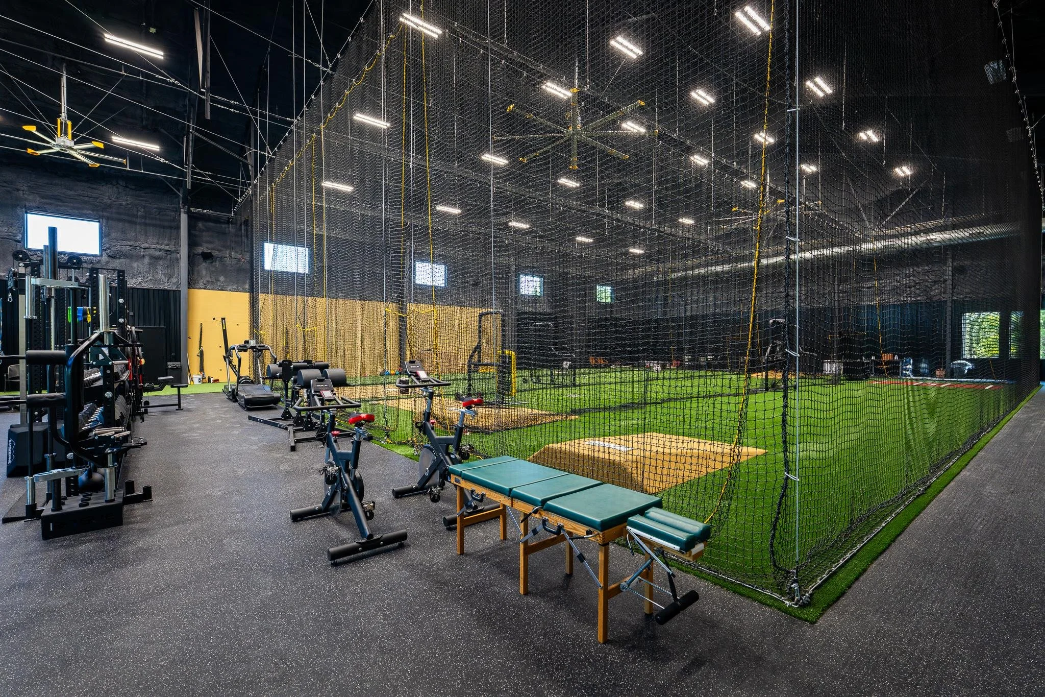 Professional indoor training facility with turf field, batting cages, cardio machines, and strength equipment in high-performance gym