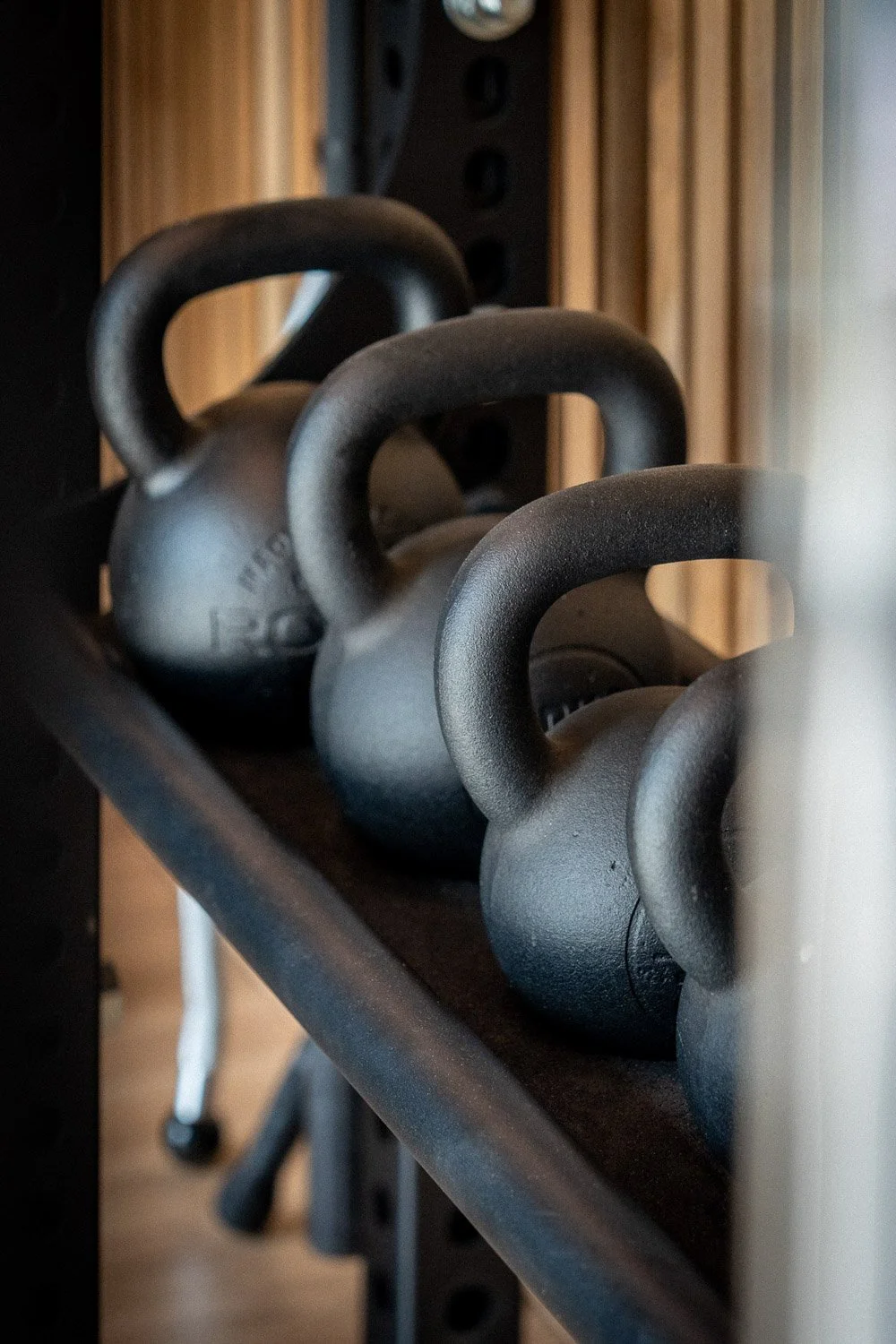 Close-up of kettlebells on storage rack in a modern custom home gym with warm wood paneling