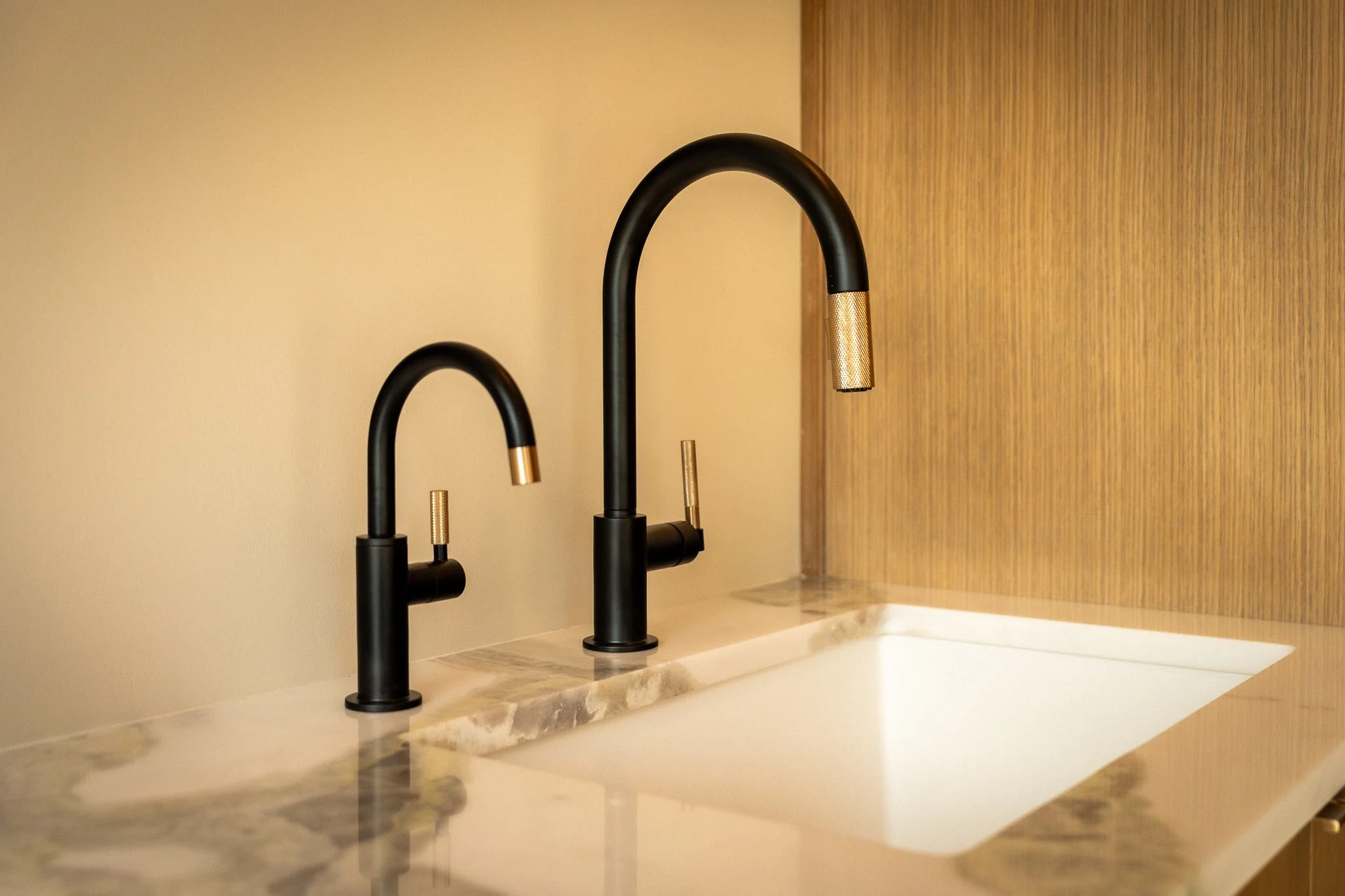 Close-up of matte black and brass faucet fixtures with marble countertop in high-end custom home gym refresh area