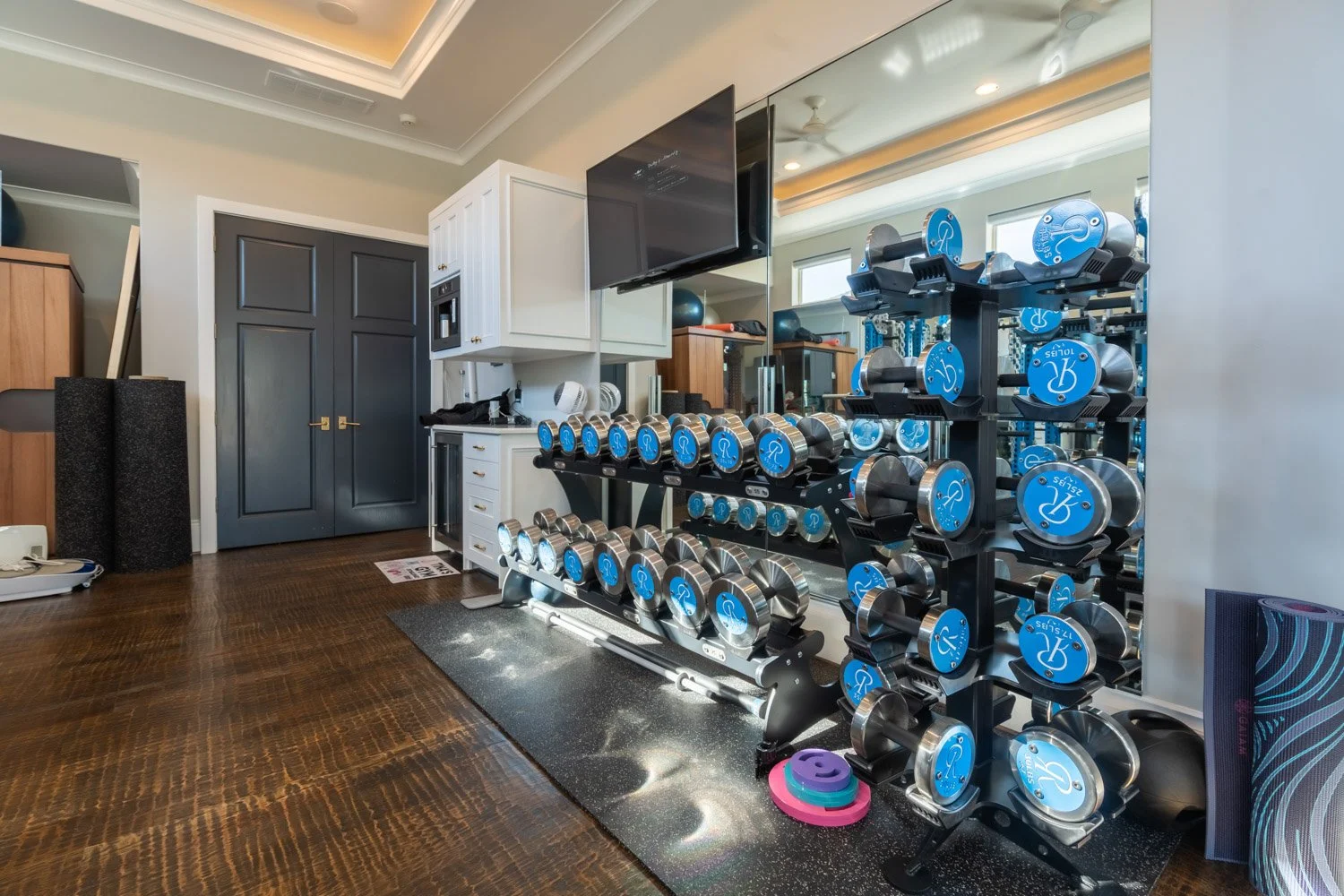 Luxury custom home gym with mirrored walls, full dumbbell rack, and organized strength training area