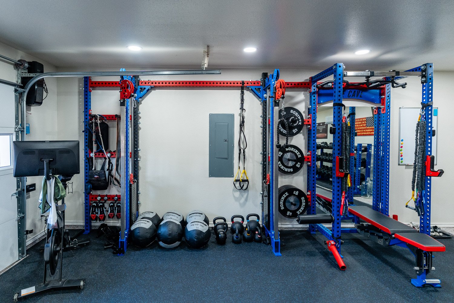 Custom home gym with dual Sorinex strength racks, Peloton bike, medicine balls, kettlebells, and organized functional training space