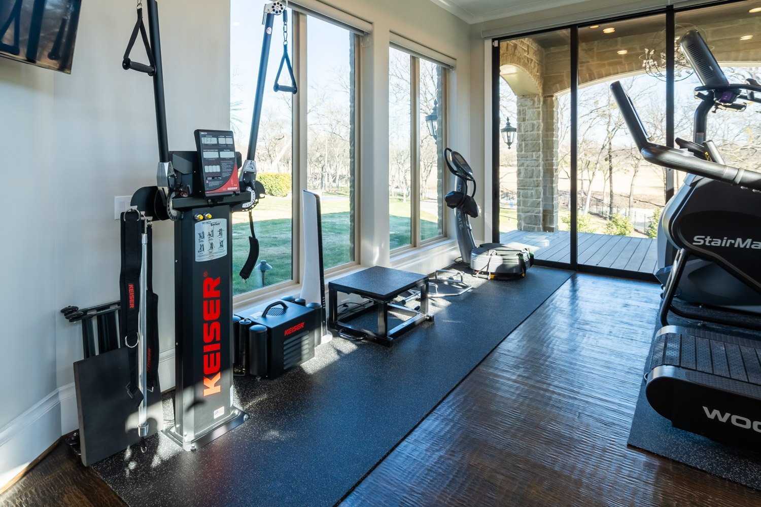 Modern home gym with Keiser functional trainer, stair climber, and treadmill in bright space with large windows