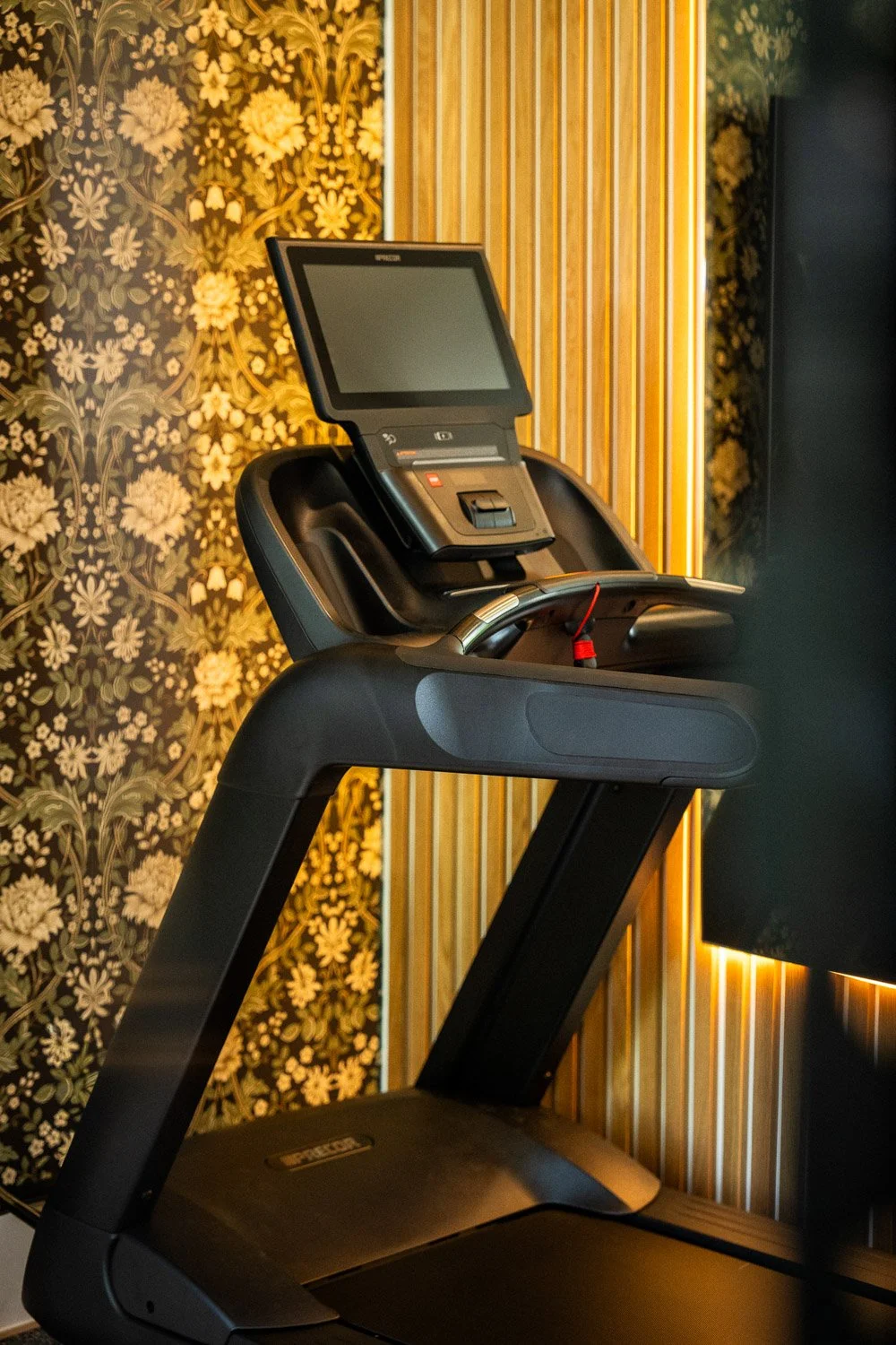 Precor treadmill in luxury home gym with decorative wallpaper and warm wood slat wall design