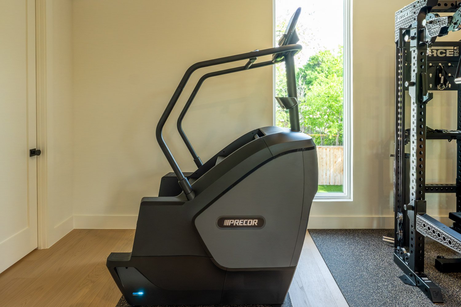 Precor stair climber in bright custom home gym with natural light and modern wood flooring