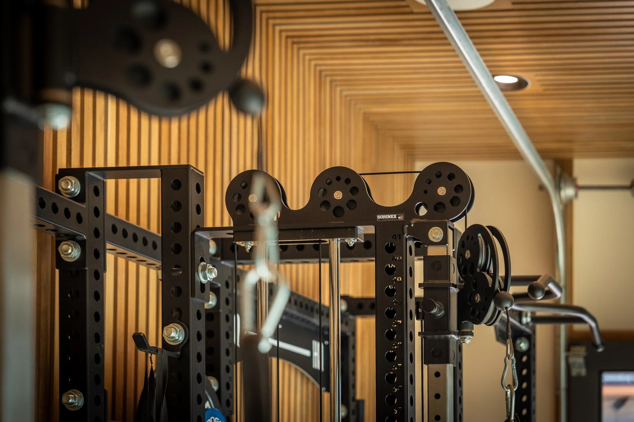 Close-up of Sorinex cable machine system with pulley attachments in custom home gym featuring wood slat design