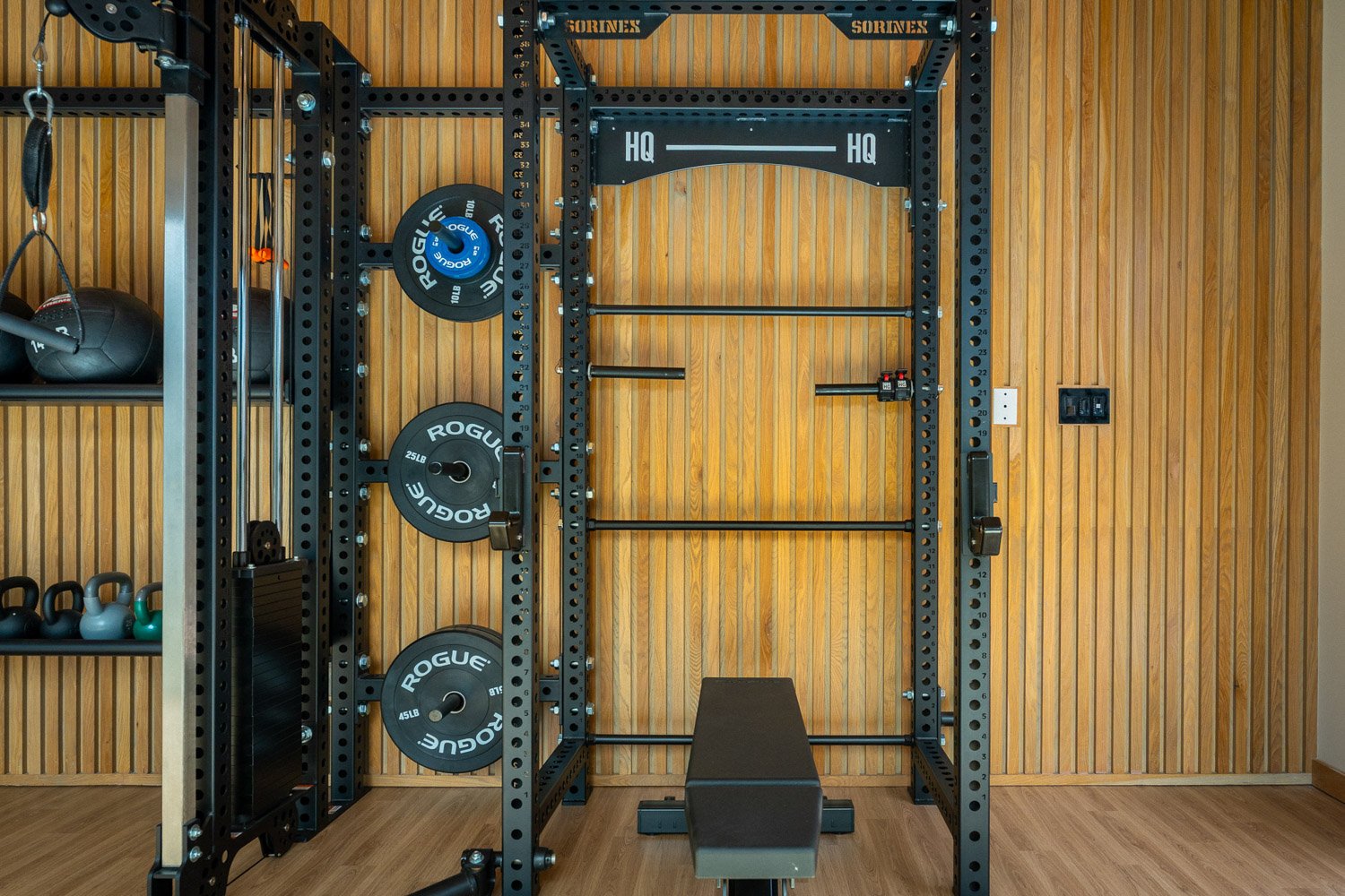 Custom home gym with power rack, weight plates, kettlebells, and premium strength training equipment against wood panel wall