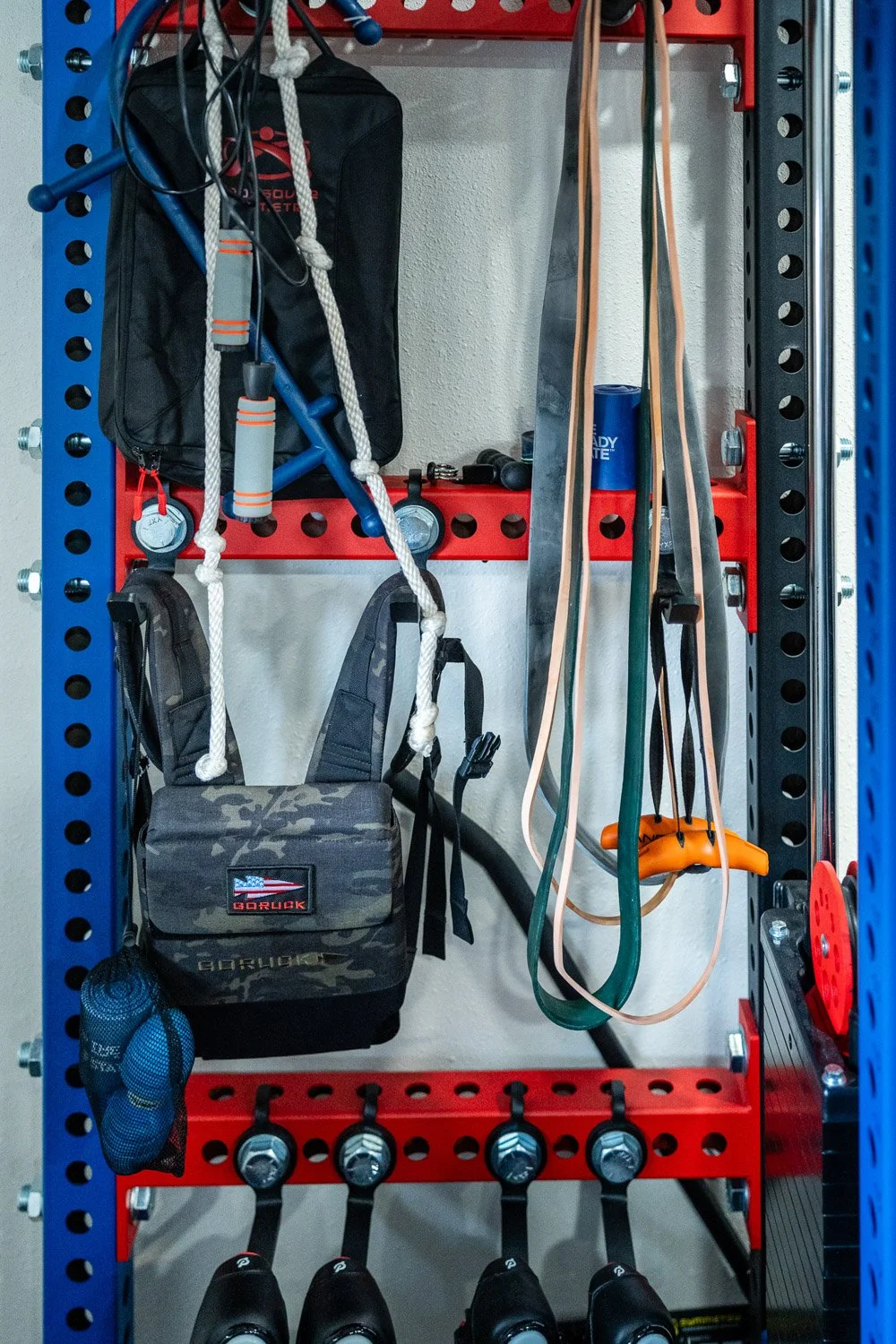 Organized gym storage with resistance bands, jump ropes, training vest, and accessories on custom strength rack