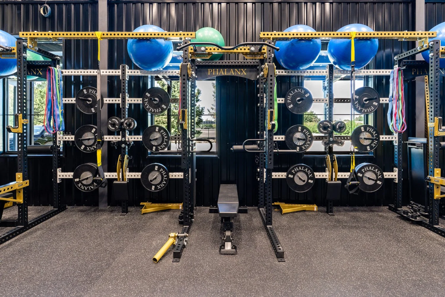 High-performance custom training gym with Phalanx strength racks, barbells, weight plates, resistance bands, stability balls, and adjustable bench in a modern functional fitness space