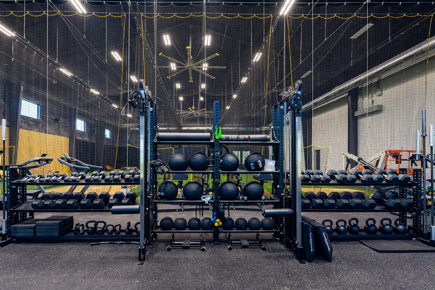 Organized strength training area with dumbbell racks, kettlebells, medicine balls, and functional fitness equipment in large gym space