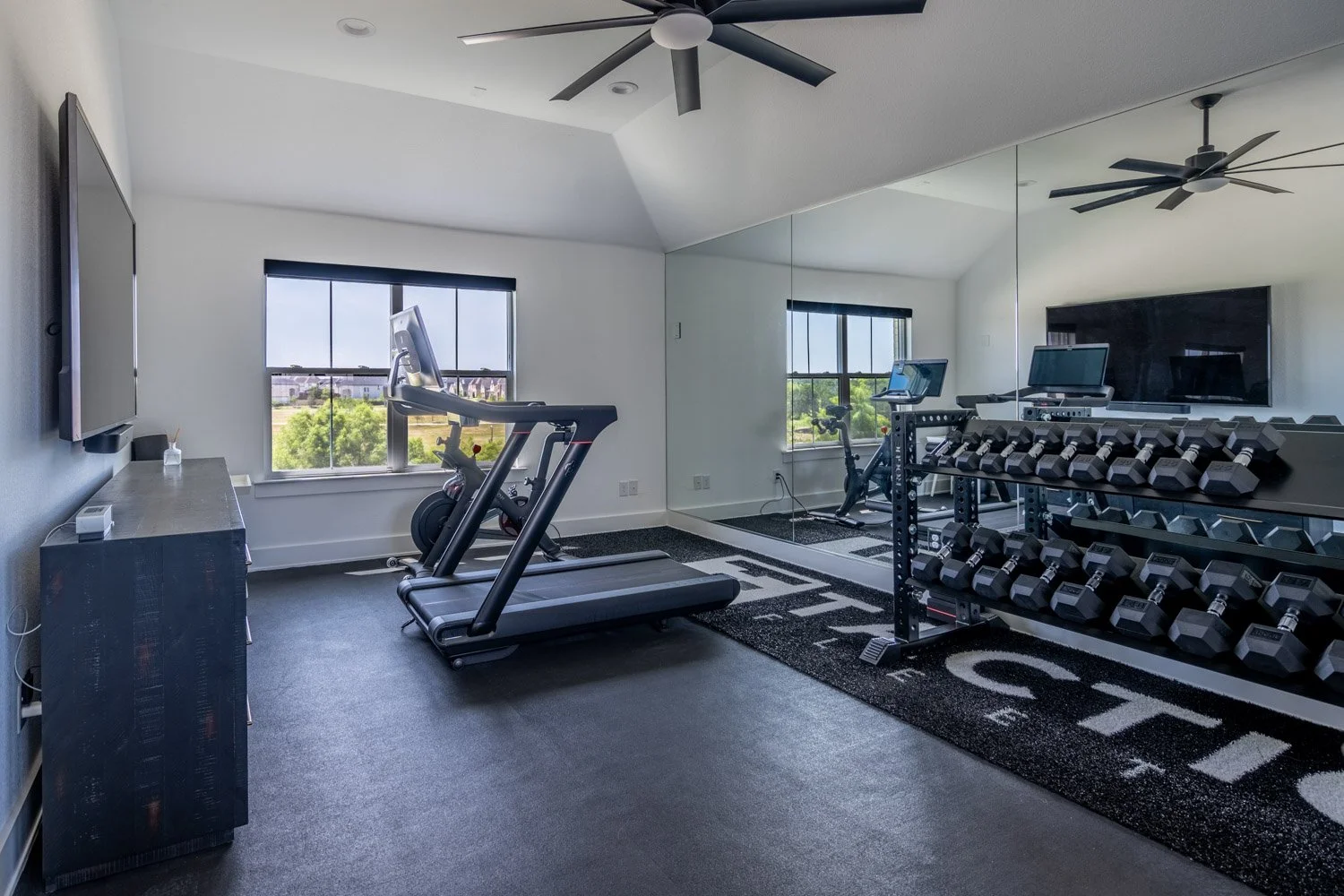 Spacious custom home gym with treadmills, Peloton bike, full dumbbell rack, mirrored wall, and sleek modern design