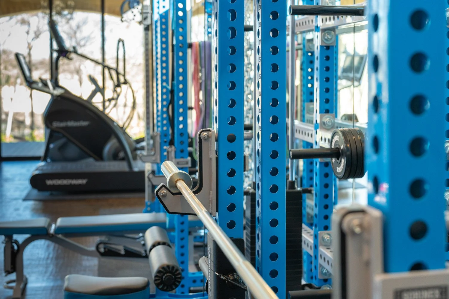 Close-up of blue custom power rack with barbell, weight storage, and strength training setup in modern home gym
