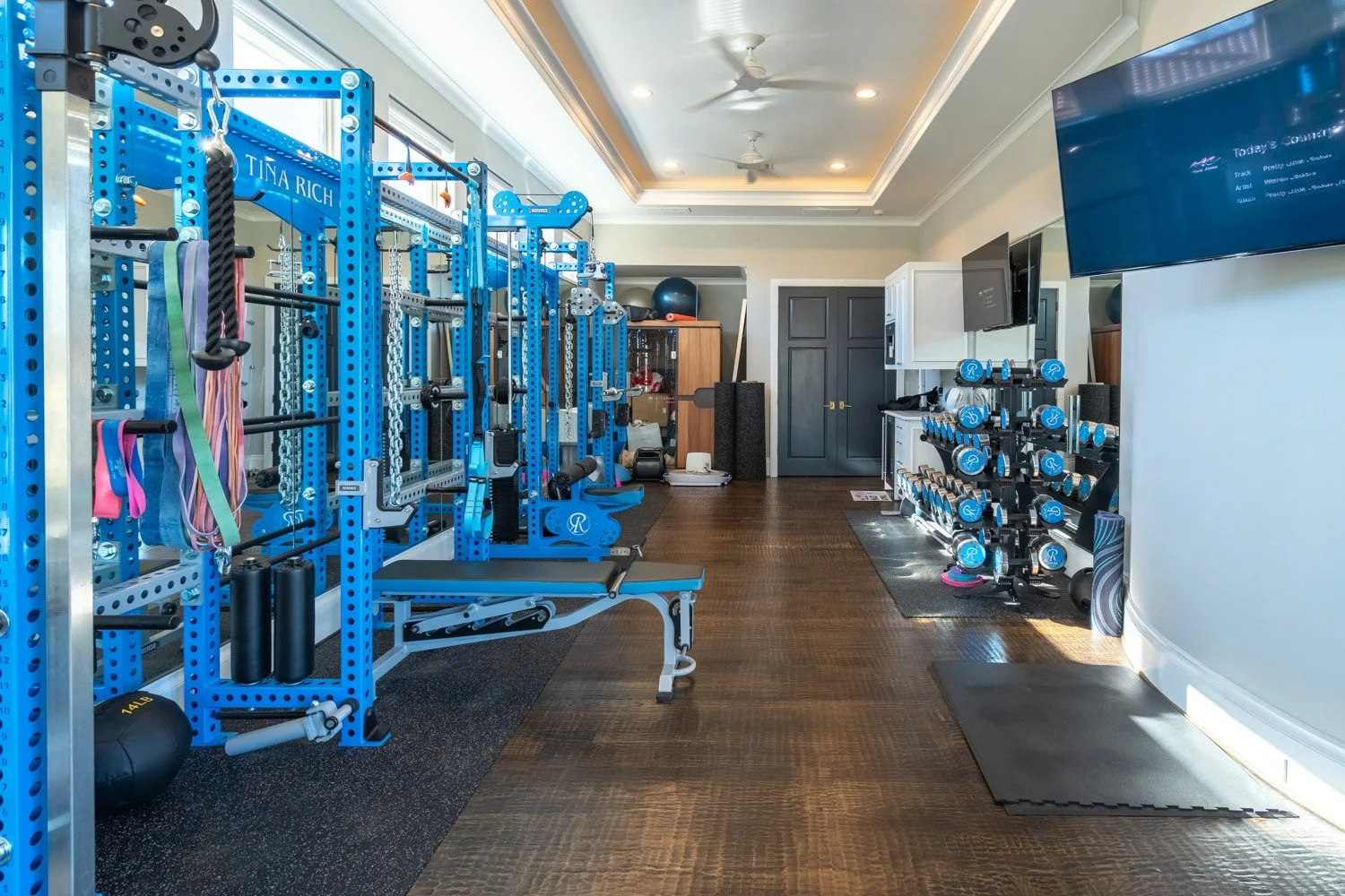 Spacious luxury home gym with blue strength equipment, full dumbbell rack, mirrors, and dedicated workout zones