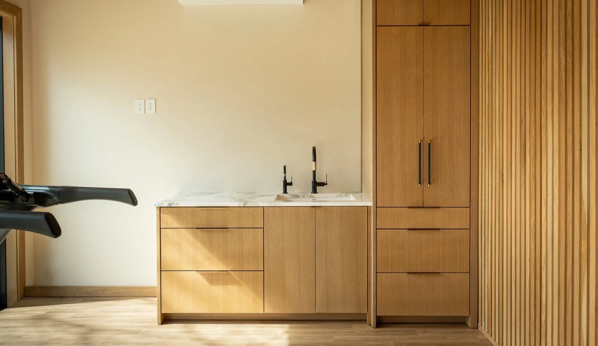 Modern home gym kitchenette with wood cabinetry, marble countertop, sink, and integrated storage in luxury fitness space
