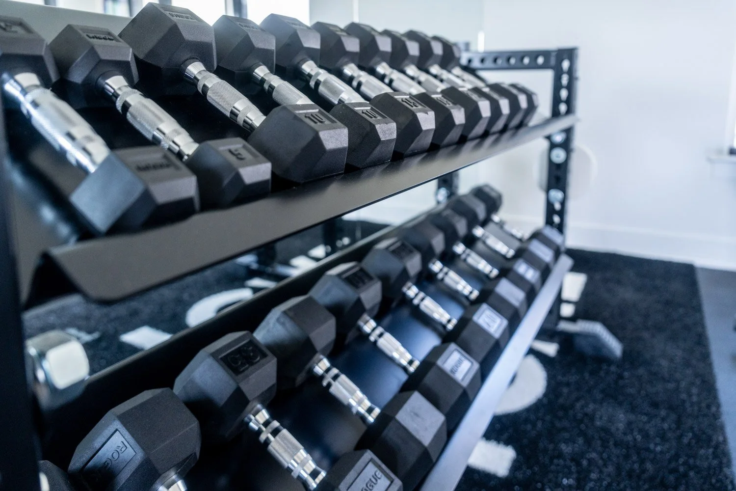 Rogue squat rack with barbell and adjustable bench in minimalist custom home gym with black rubber flooring