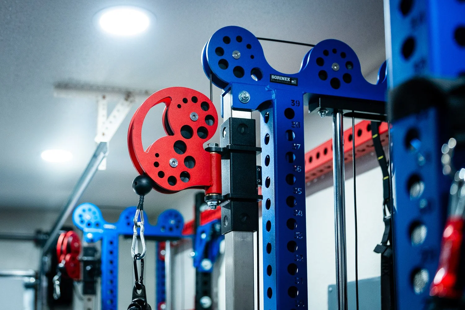 Detail of custom cable pulley system on red and blue power rack with Sorinex strength equipment