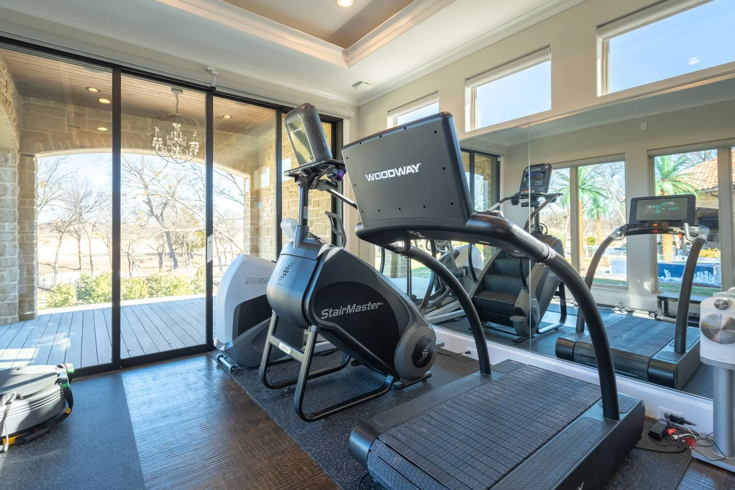 High-end home gym with Woodway treadmill, StairMaster, and cardio equipment in bright space with large windows