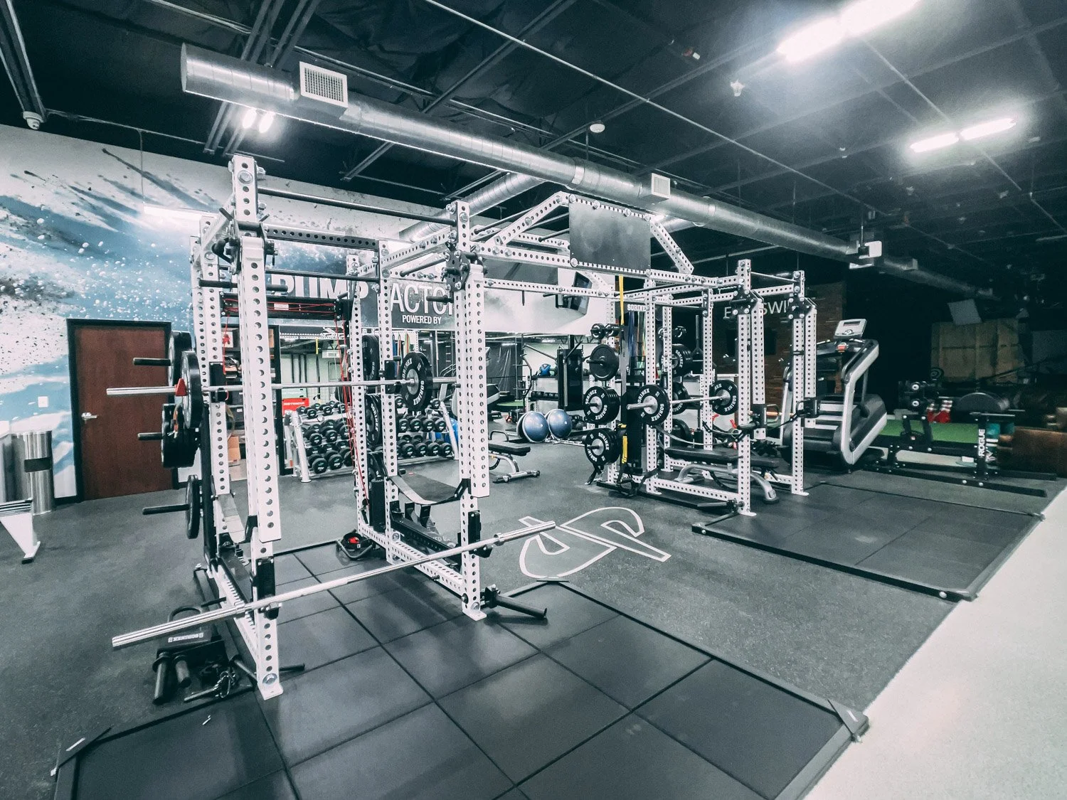 Large custom training gym with Sorinex strength racks, barbells, weight plates, rubber flooring, and dedicated functional workout zones in professional fitness facility