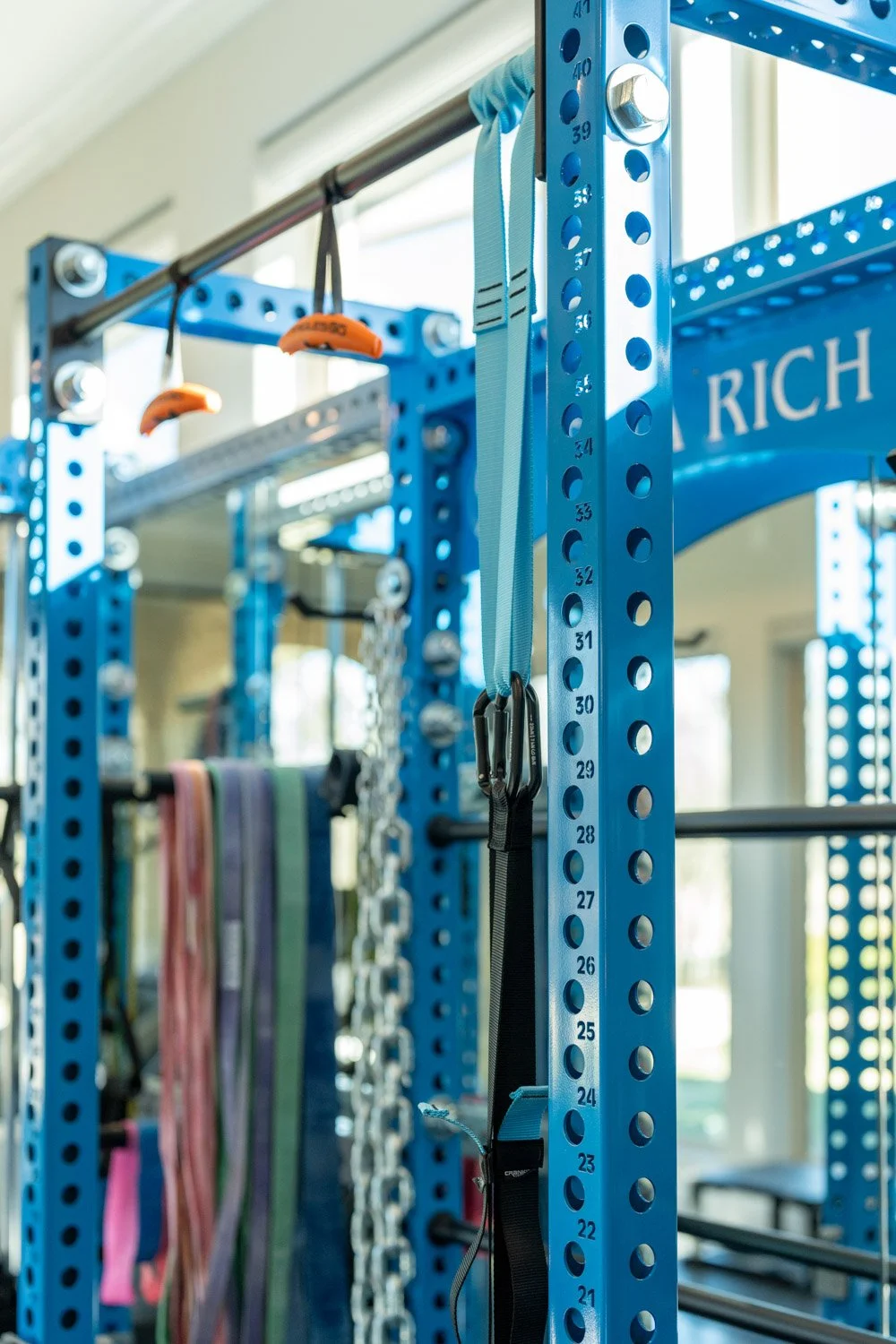 Detailed view of blue power rack with suspension straps, pull-up bar, and functional training accessories in home gym