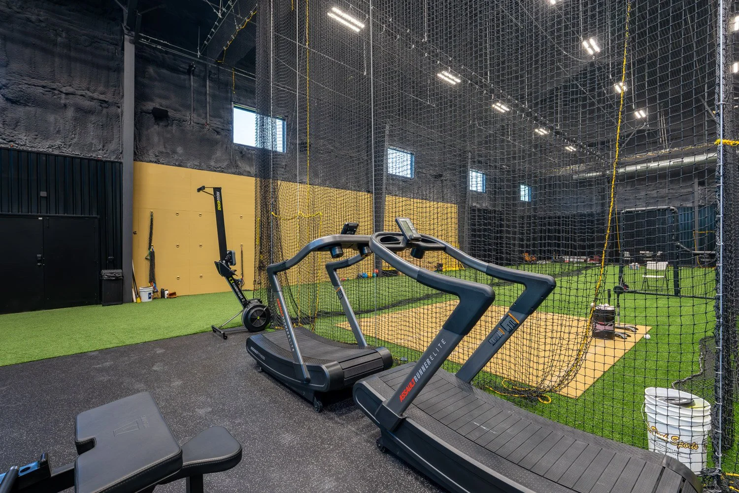 AssaultRunner treadmills next to indoor turf field and netted batting cage in professional training gym