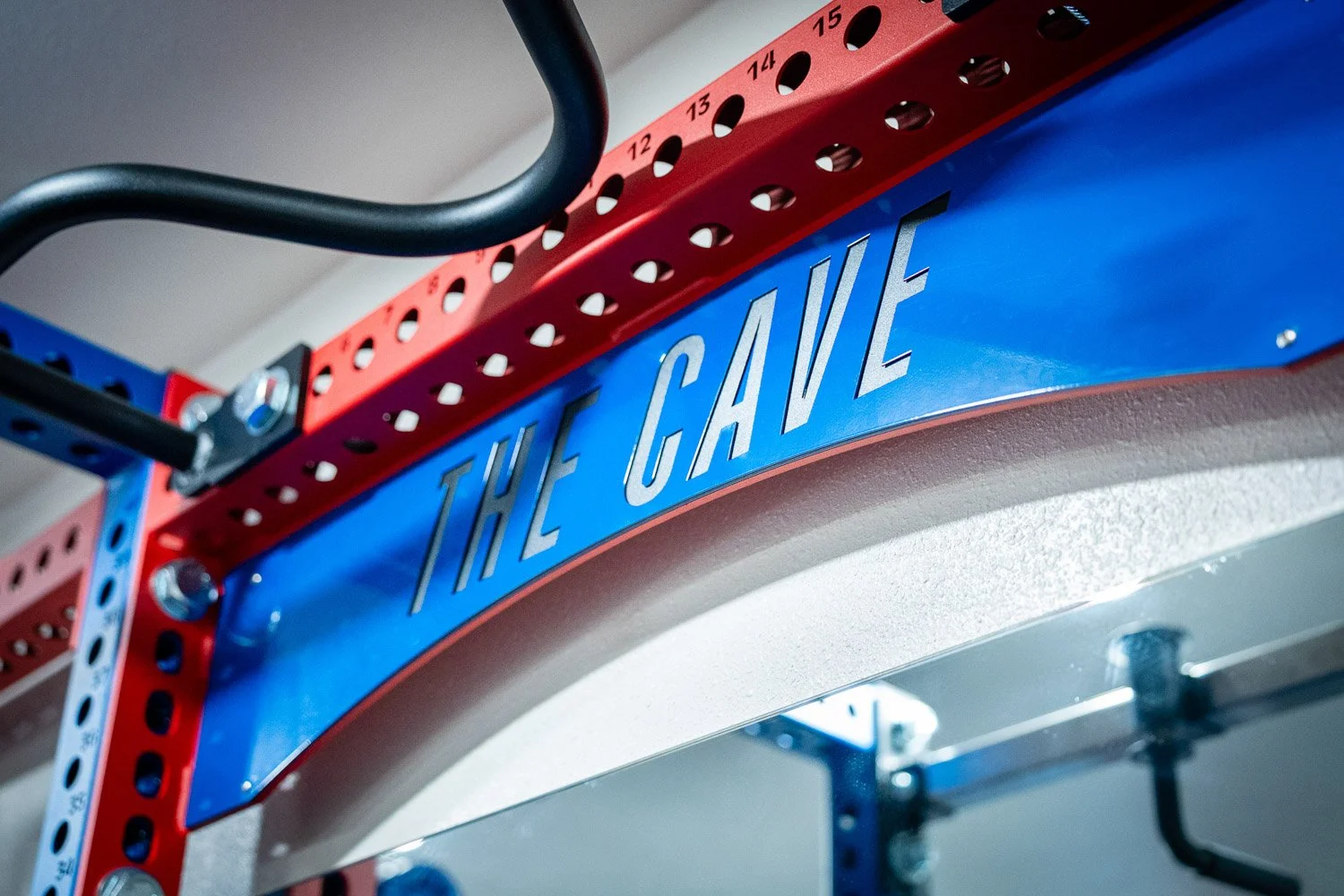 Close-up of custom home gym power rack with ‘The Cave’ signage in red and blue steel strength equipment