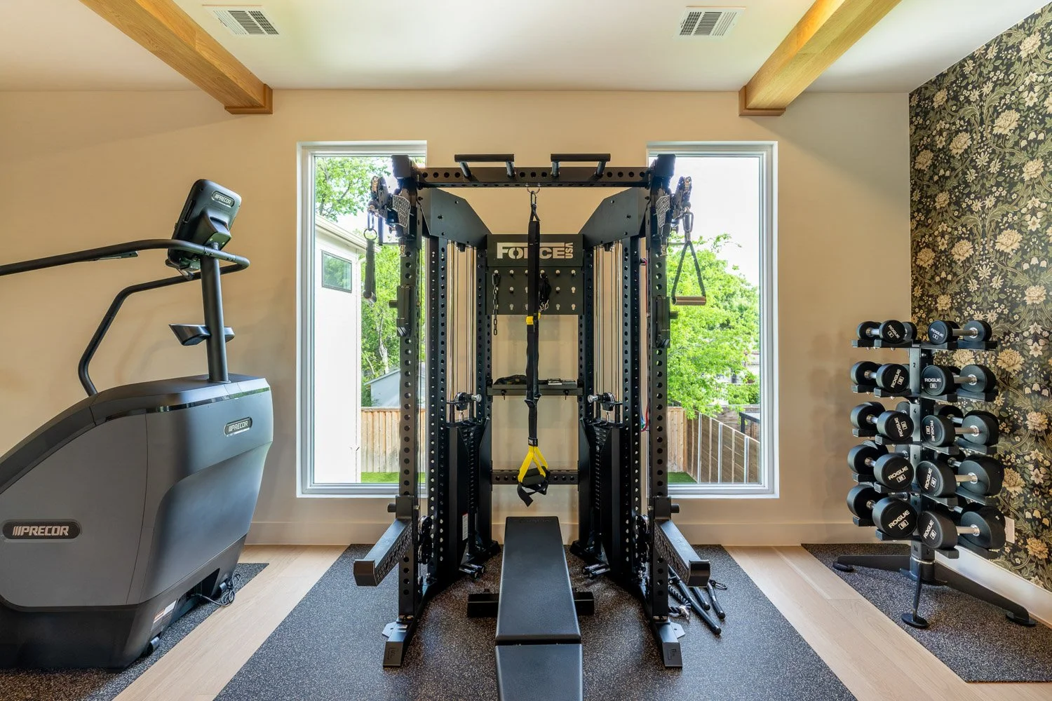 Custom home gym featuring Force USA training system, Precor stair climber, Rogue dumbbells, and balanced layout between large windows