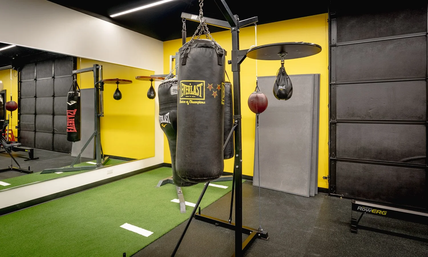Luxury home boxing gym with Everlast heavy bags, speed bag platform, turf training area, and custom fitness design