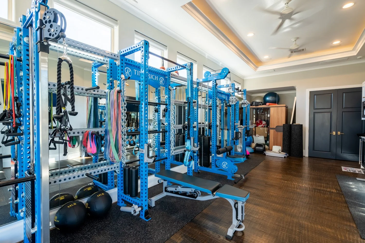 Custom home gym with blue multi-station strength rack, resistance bands, adjustable bench, and mirrored training space