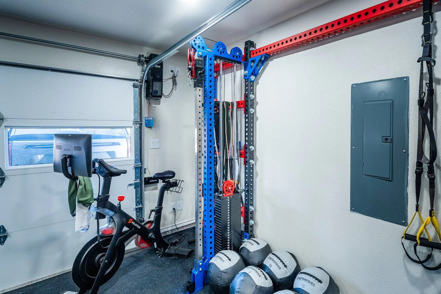Compact custom home gym with Peloton bike, cable machine, medicine balls, and wall-mounted suspension trainer