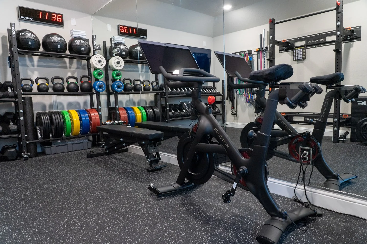 Compact luxury home gym with Peloton bike, kettlebells, dumbbells, and organized Rogue fitness equipment