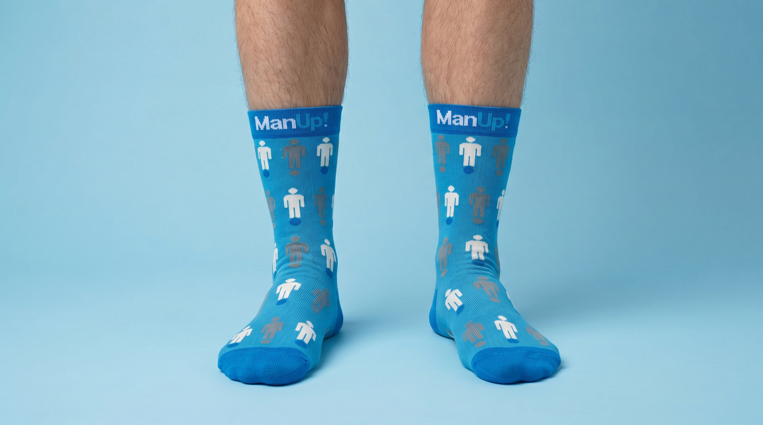 Pair of legs wearing blue socks with white and gray human icons and the text 'ManUp!' on the socks, standing against a light blue background.