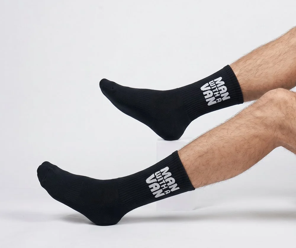 Person wearing black socks with white text reading "Man With A Plan", legs extended against a plain gray background.