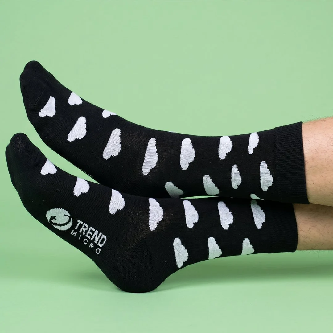 Pair of black socks with white heart patterns and the brand name 'TREND MICRO' on a person's feet against a light green background.